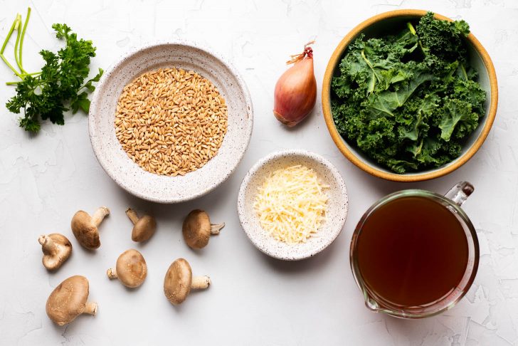 Mushroom and kale farro risotto ingredients measured out on a light grey backdrop