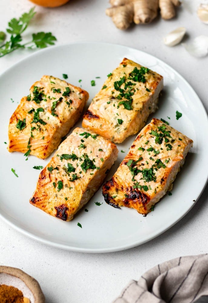 4 pieces of cooked salmon on a dinner plate garnished with chopped cilantro