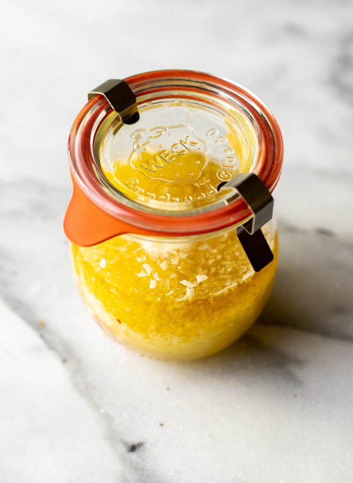 Jar of parmesan lemon vinaigrette on a white marble surface