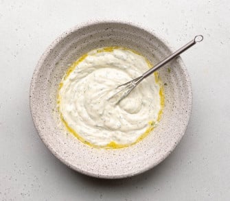 whisked up greek yogurt dressing in a speckled bowl with a small whisk