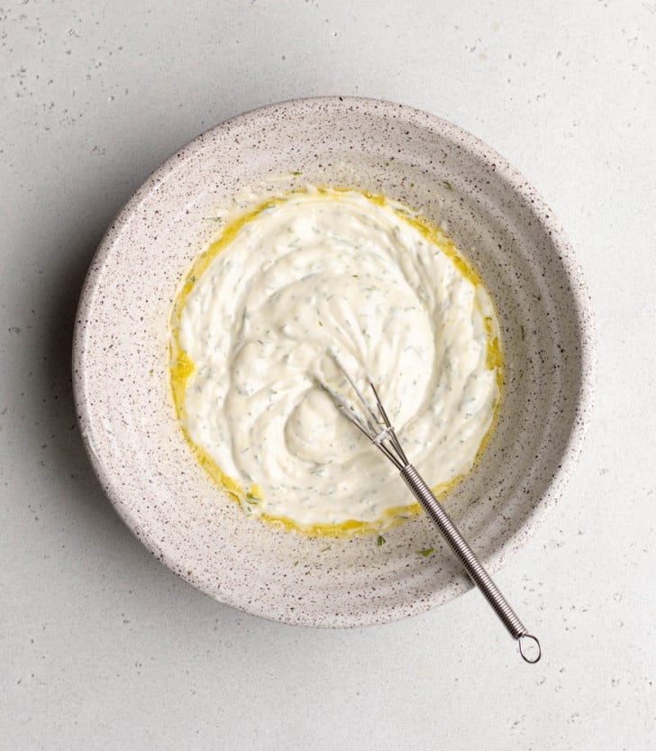 whisked up greek yogurt dressing in a speckled bowl with a small whisk