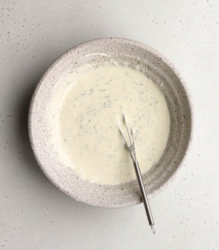 greek yogurt salad dressing in a speckled bowl with a small whisk