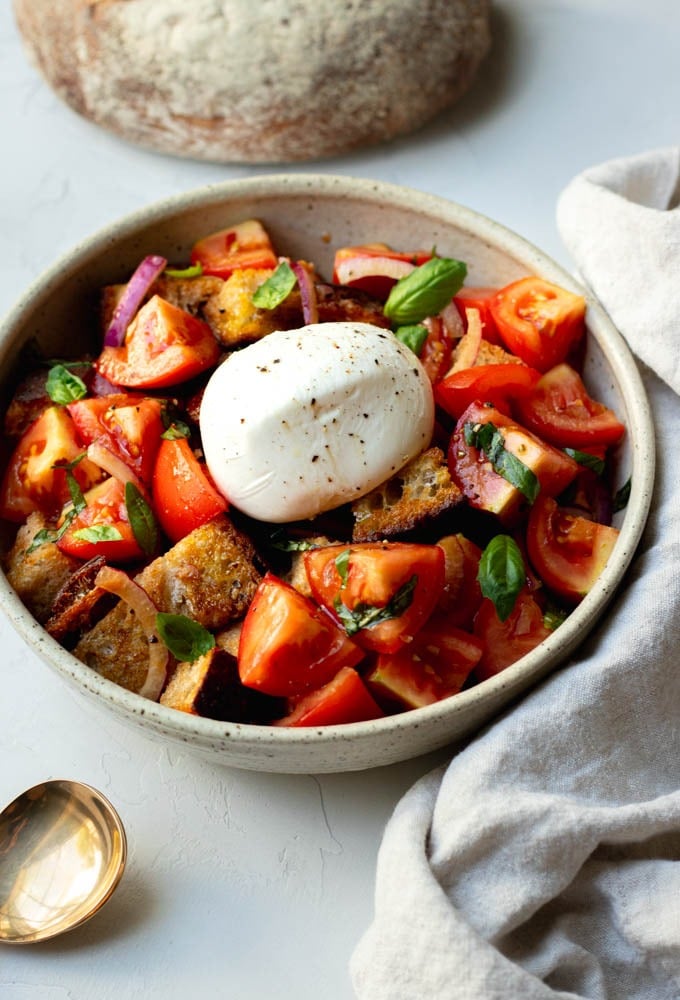 Close up of a bowl of burrata panzanella salad in a speckled bowl on a grey backdrop