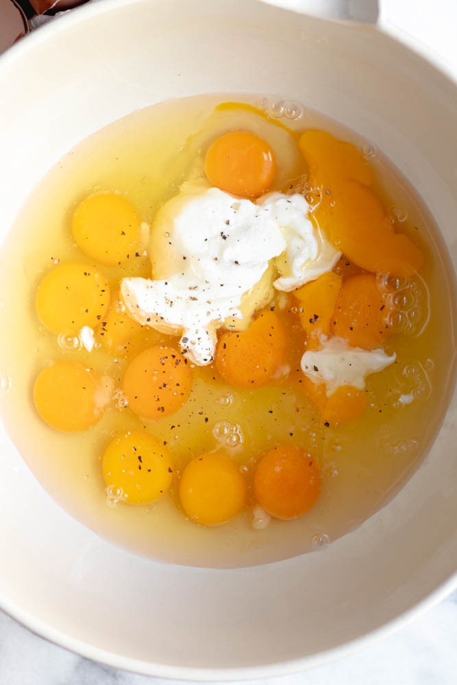 Dozen eggs in a mixing bowl before being whisked with Greek yogurt, salt, and pepper to make mini frittatas