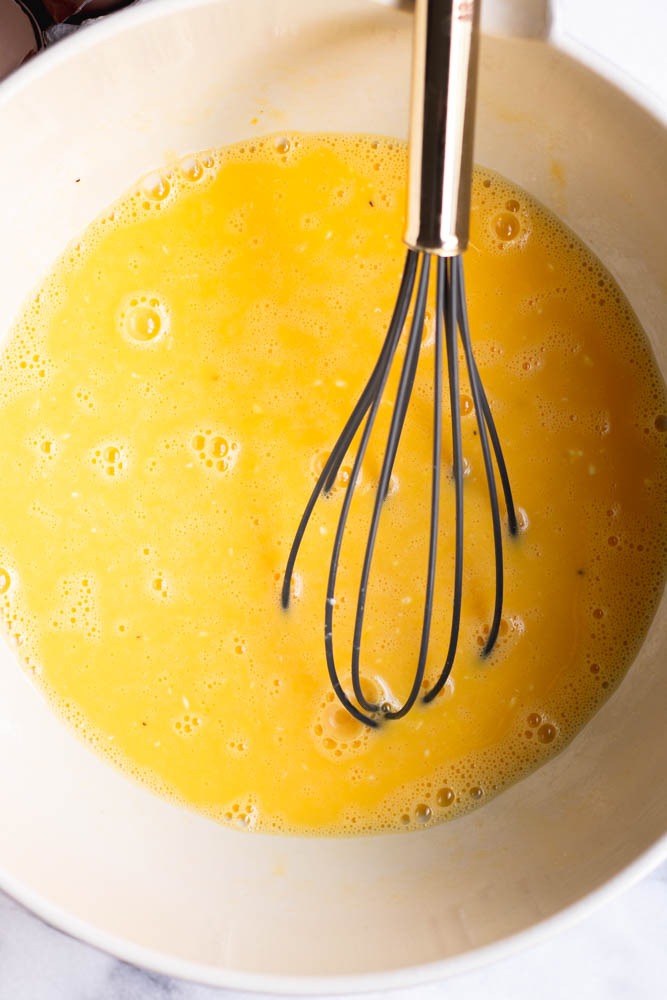 Whisked eggs in a mixing bowl with a whisk