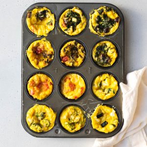 12 mini frittatas in a muffin tin with different veggies and cheese