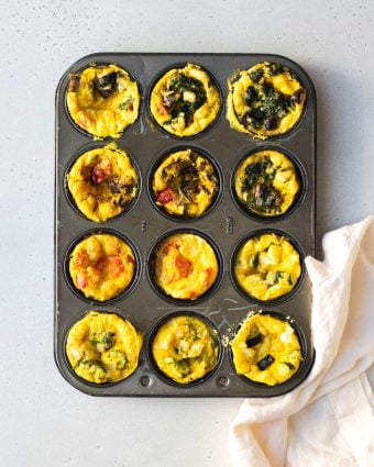 12 mini frittatas in a muffin tin with different veggies and cheese