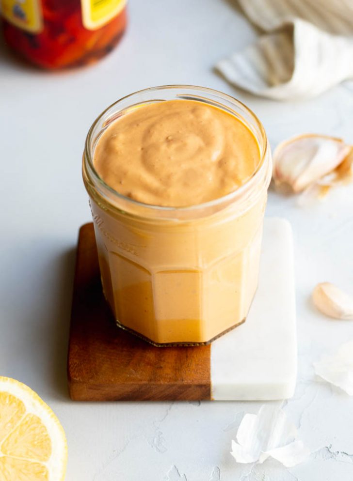 Jar of roasted red pepper tahini sauce on a coaster with ingredients surrounding the jar
