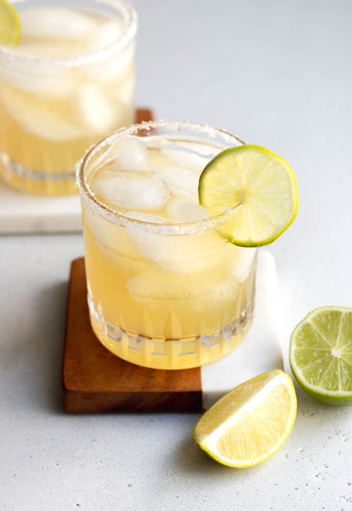 Mezcal margarita in a rocks glass garnished with lime slice and salted rim sitting on a wooden/marble coaster
