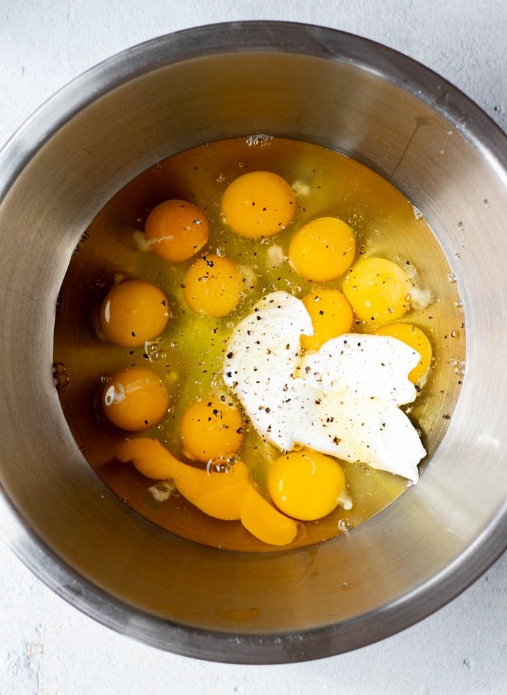 a dozen eggs cracked into a mixing bowl with a scoop of yogurt