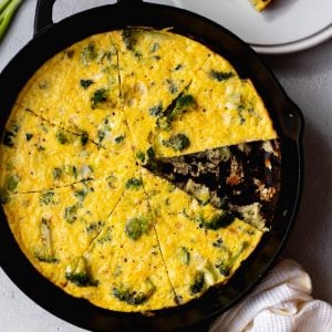 broccoli frittata sliced in a cast iron skillet with one serving on a plate beside it