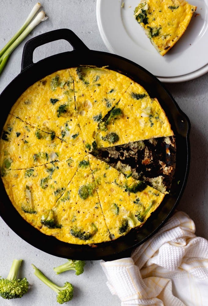 broccoli frittata sliced in a cast iron skillet with one serving on a plate beside it