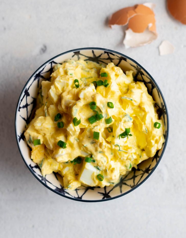 Small bowl of egg salad on a light grey backdrop