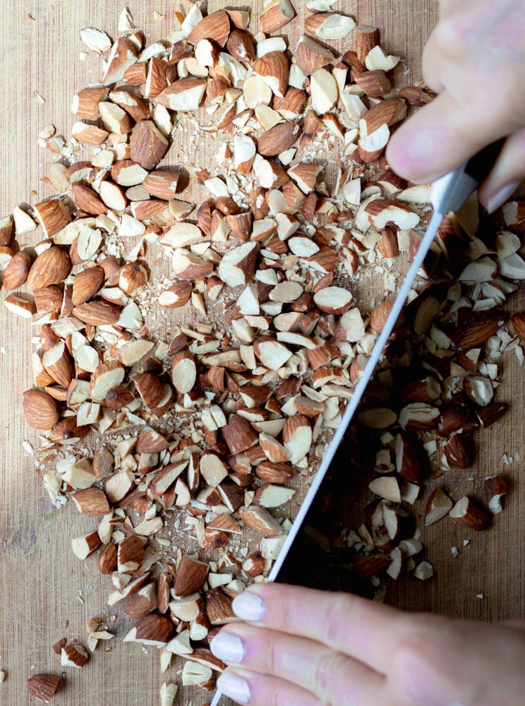 hands chopping up almonds on a wooden cutting board