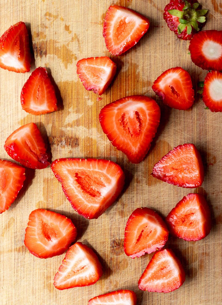 strawberries cut in half on a wooden cutting board