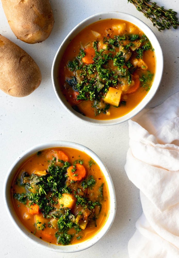 two bowls of carrot potato soup on a light grey backdrop