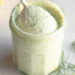jar of creamy feta dill dressing on a grey backdrop with a spoon
