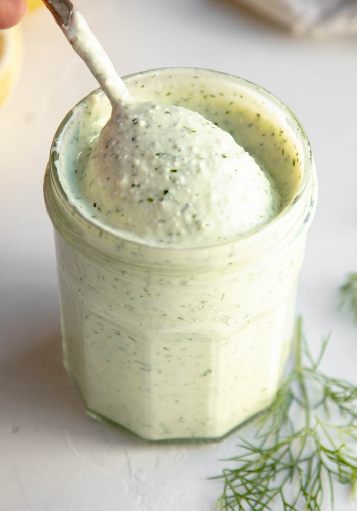jar of creamy feta dill dressing on a grey backdrop with a spoon