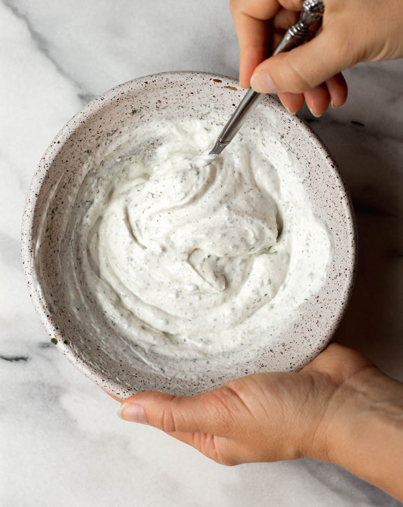 hand mixing up Greek yogurt ranch dip in a speckled mixing bowl