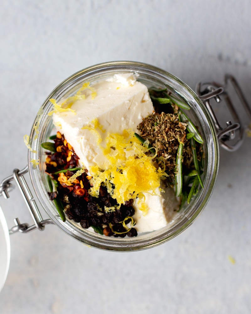 cubes of feta cheese, rosemary, lemon zest, and spices in a small jar