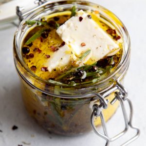 marinated feta cheese in a small jar on a light grey surface