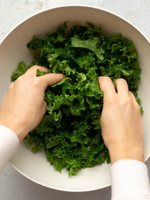 hands massaging curly kale in a white bowl