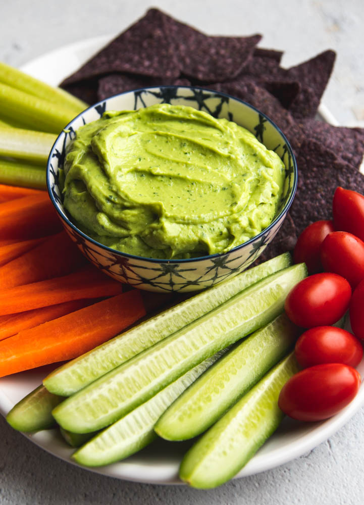 Bowl of avocado greek yogurt dip surrounded by veggies and chips