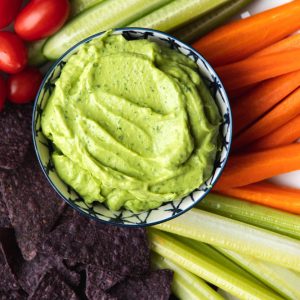 Bowl of avocado greek yogurt dip surrounded by veggies and chips