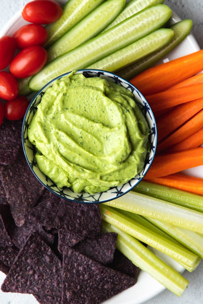 Bowl of avocado greek yogurt dip surrounded by veggies and chips