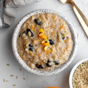 small bowl of brown rice pudding garnished with orange peel on a light grey backdrop