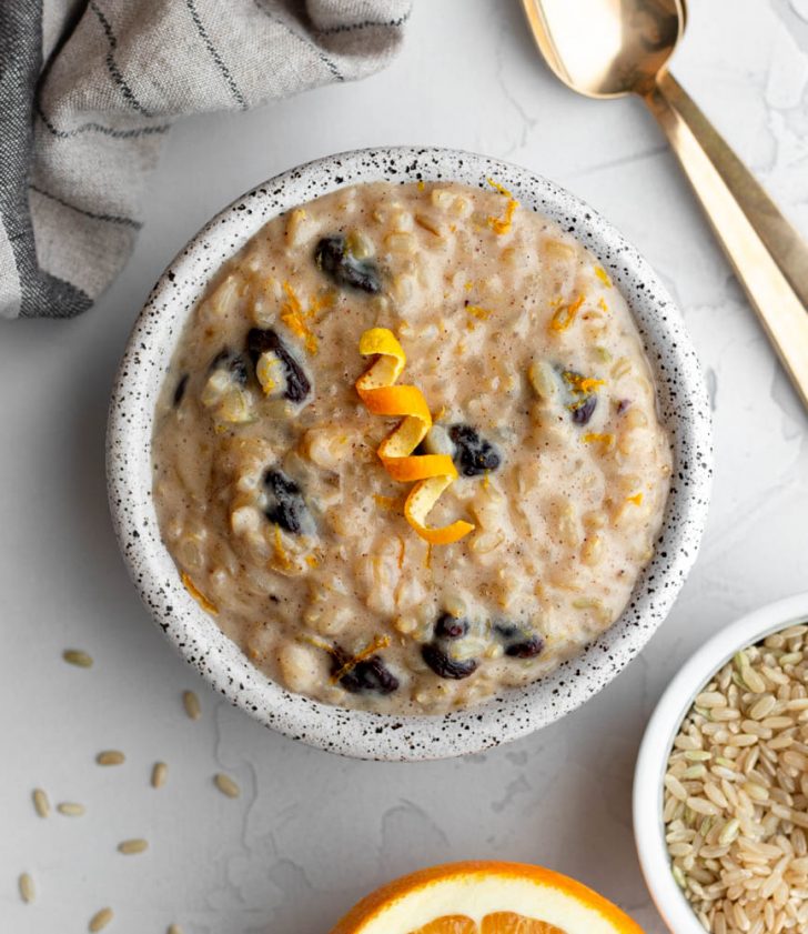 small bowl of brown rice pudding garnished with orange peel on a light grey backdrop