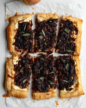 sliced puff pastry tart with balsamic caramelized onions on a piece of white parchment paper