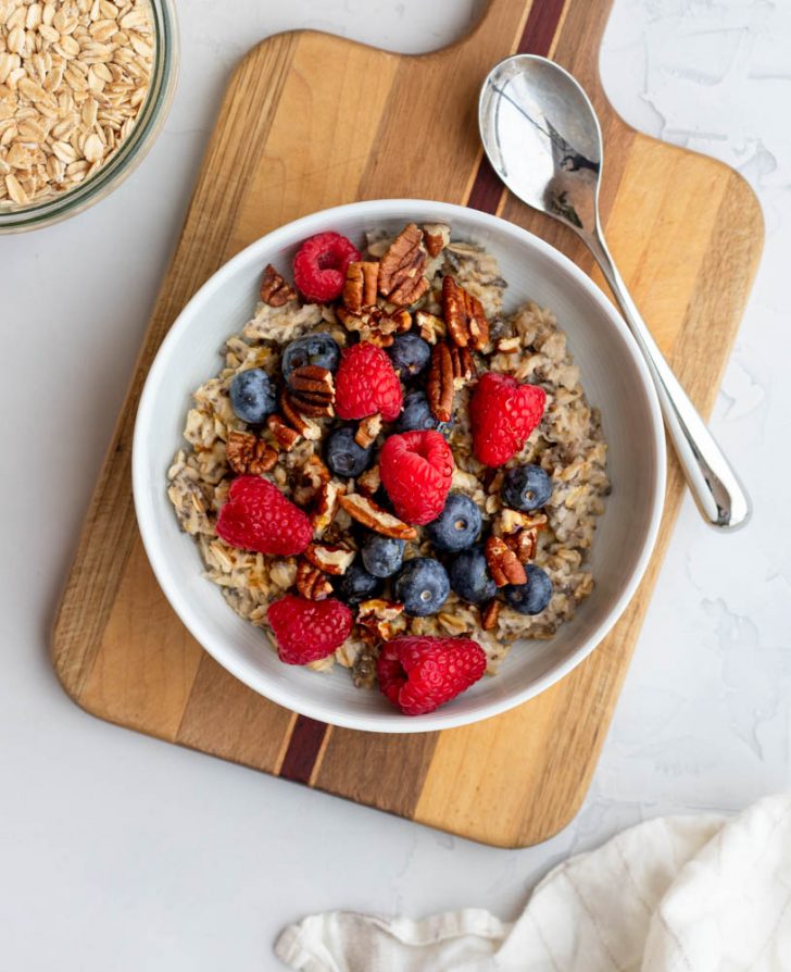 Bowl of oatmeal topped with berries and nuts on a wooden cutting board
