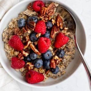 Bowl of oatmeal topped with berries and nuts, with a spoon