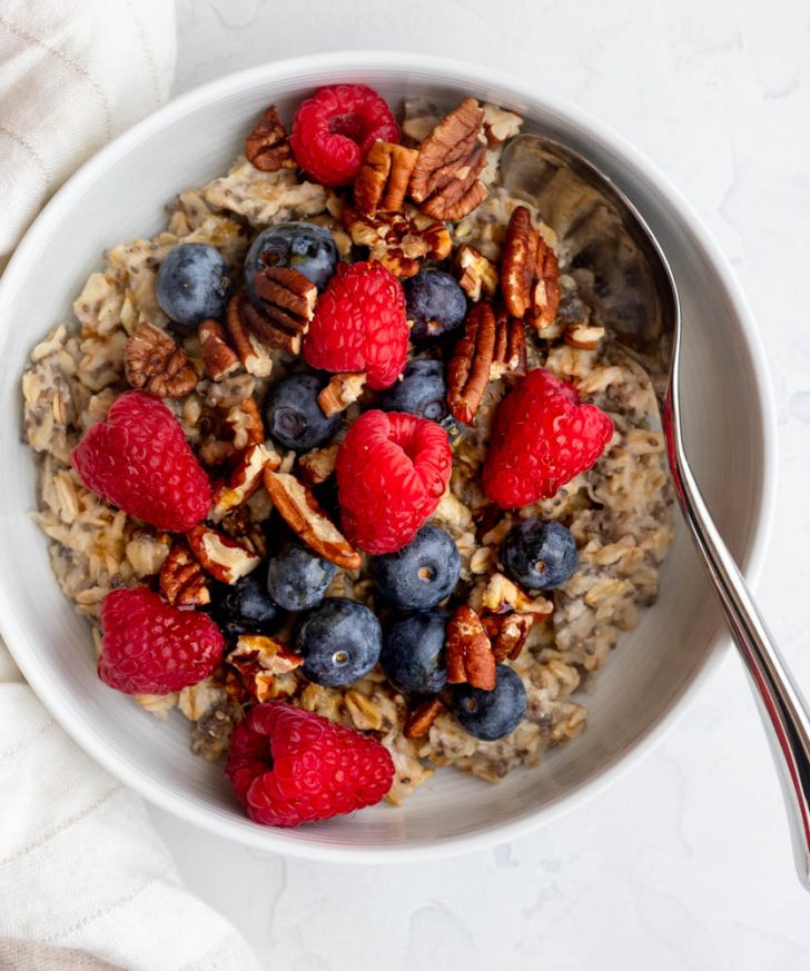Bowl of oatmeal topped with berries and nuts, with a spoon
