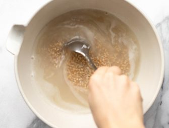 hand stirring up a bowl of oatmeal being cooked in a white bowl