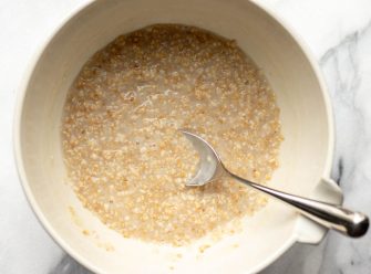 White bowl with cooked oatmeal with a silver spoon