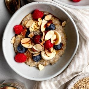 bowl of steel cut oatmeal topped with sliced almonds and berries, surrounded by small bowls of ingredients, a striped dish towel, and a spoon