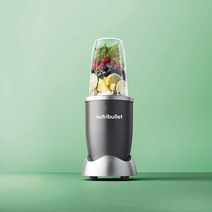 NutriBullet personal blender filled with fruit against a green backdrop