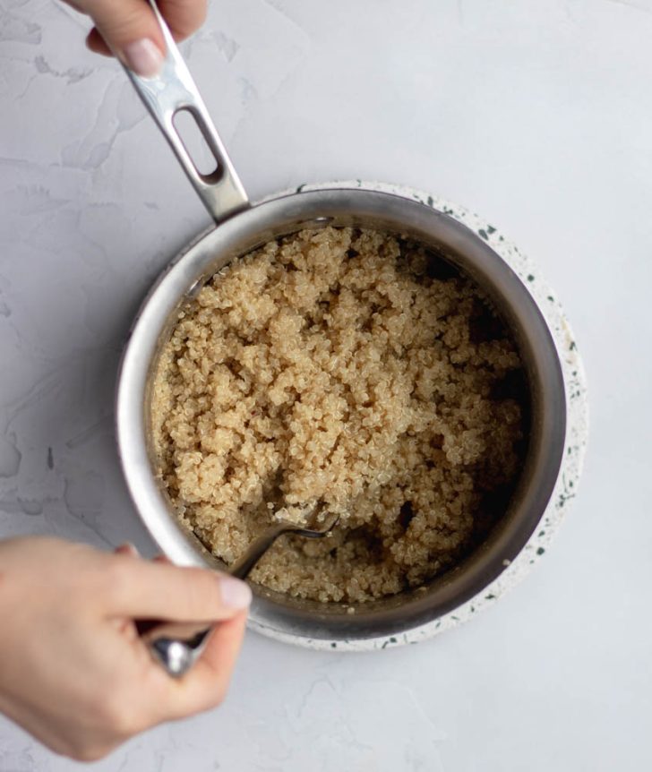 hand fluffing a pot of cooked quinoa with a fork