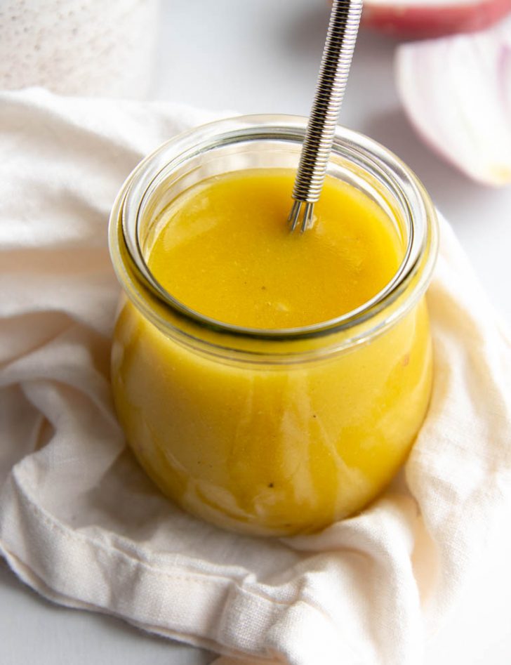 glass jar filled with white balsamic vinaigrette and a spoon on a white dish towel
