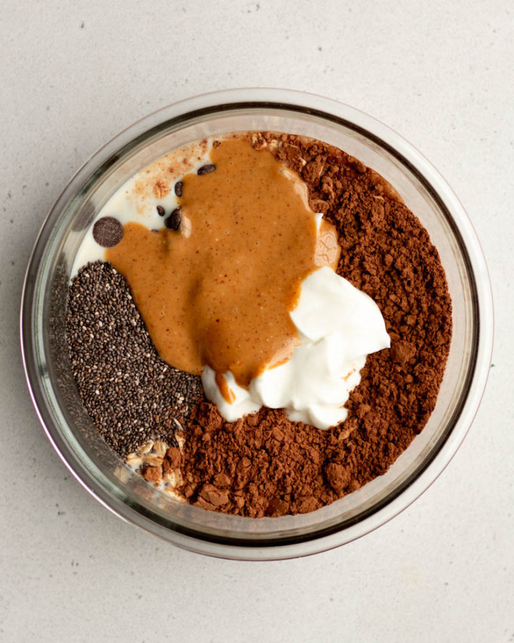 chocolate peanut butter overnight oats ingredients in a glass circular container before being mixed 