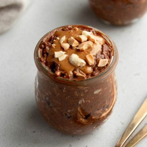 jar of chocolate peanut butter overnight oats with two gold spoons on a light grey backdrop