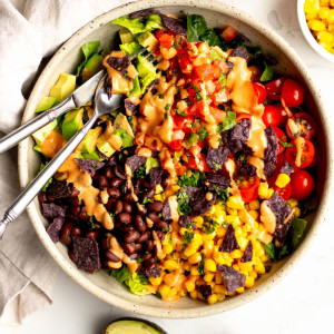 bowl of vegetarian taco salad with a fork and knife, surrounded by some ingredients on a white background