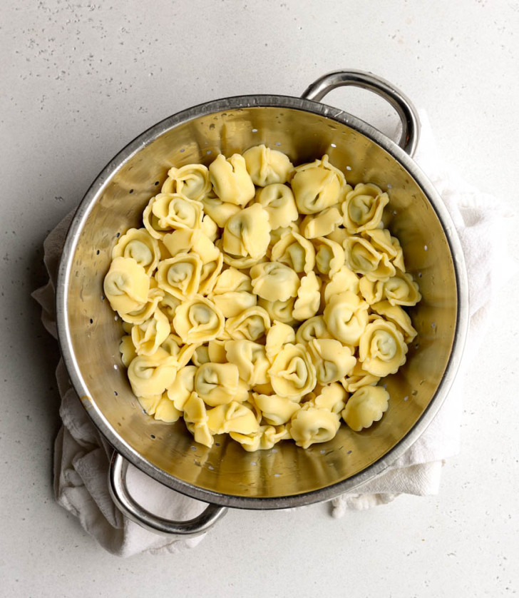 Tortellini in a metal strainer on a light grey backdrop