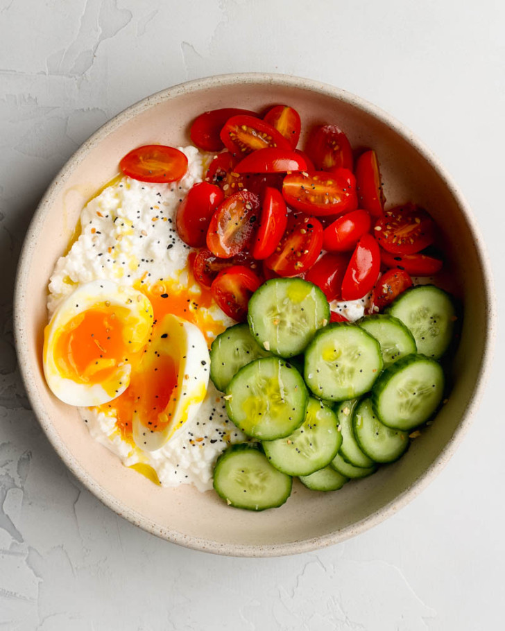 savory cottage cheese breakfast bowl with cucumber, tomatoes, and soft boiled egg on light grey backdrop 