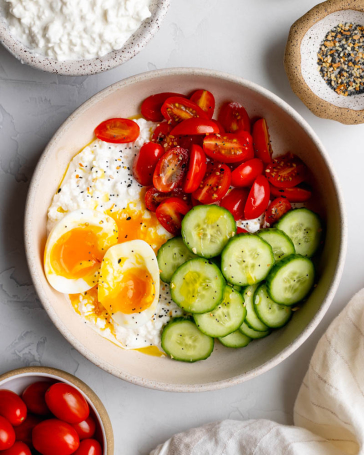 savory cottage cheese breakfast bowl on light grey backdrop surrounded by ingredients 