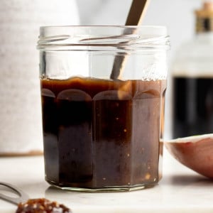 Jar of fig balsamic dressing with a spoon, with olive oil and balsamic vinegar bottles in the background