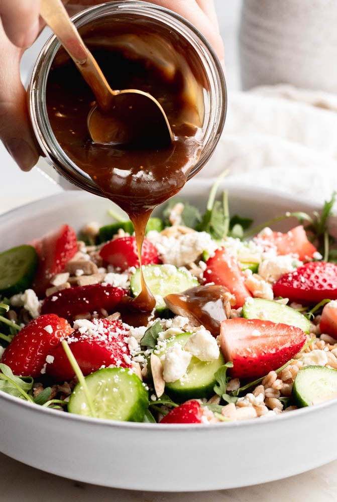 hand drizzling fig balsamic dressing over a strawberry salad