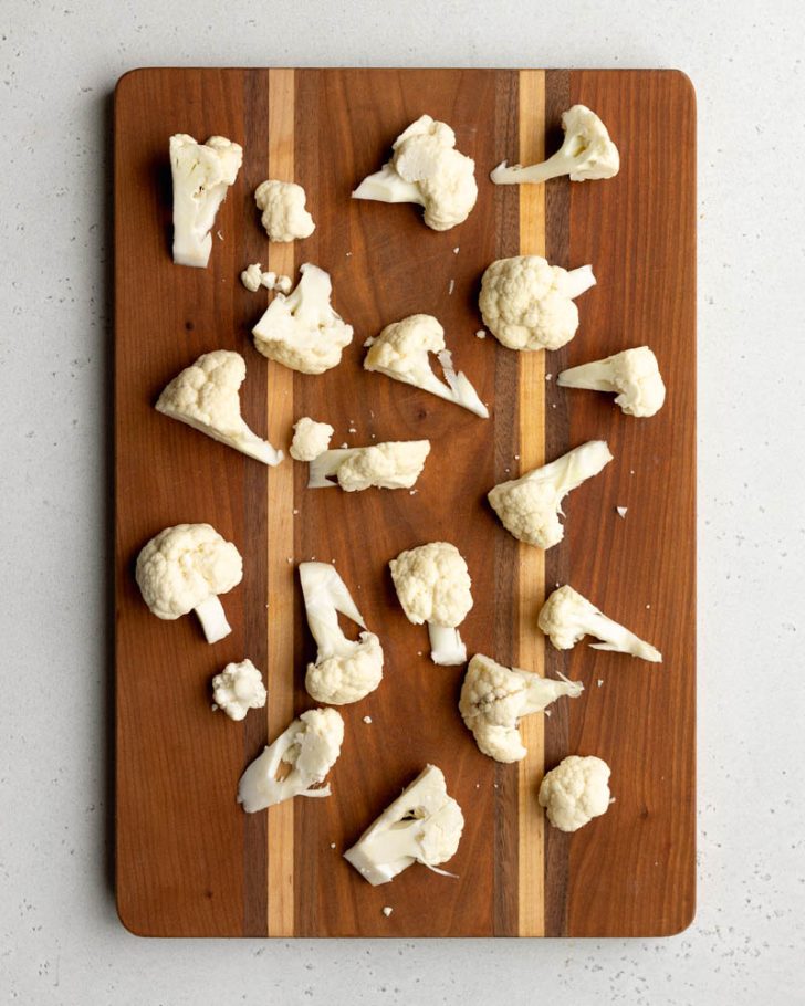 cauliflower cut into florets on wooden cutting board